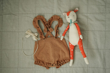 Knitted baby romper with ruffles and soft toy on neutral background, top view.