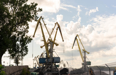Multiple port cranes and a large pile of coal at an industrial terminal under a cloudy sky