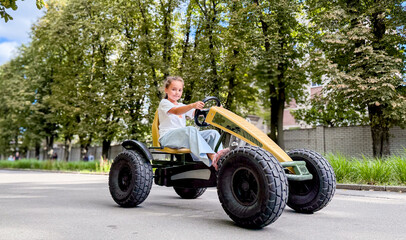 A young girl of Caucasian descent joyfully rides a go-kart on a tree-lined street, capturing a moment of childhood thrill.