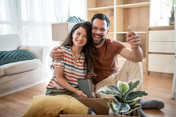 Happy couple showing new house keys while unpacking boxes in living room
