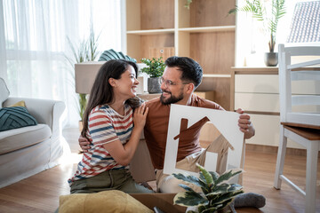 Happy couple holding house sign and smiling after moving into new home