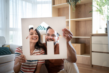 Happy couple holding a house sign and smiling in their new home