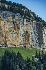 Remote Swiss mountain guesthouse nestled at the base of a towering vertical cliff, surrounded by...