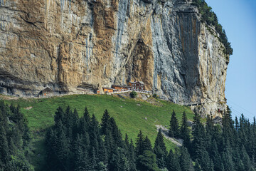 Remote Swiss mountain guesthouse nestled at the base of a towering vertical cliff, surrounded by...