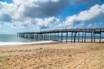Obraz premium Wooden Pier over Atlantic Ocean. Scenic beach view with clouds and surf.