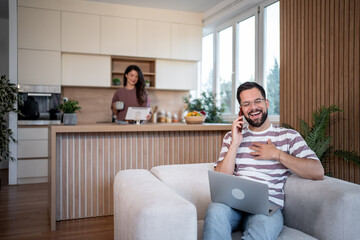 Happy freelancer talking on phone and using laptop at home