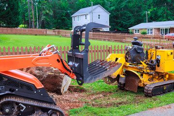 Construction equipment works on landscaping, clearing land, removing tree stumps in residential neighborhood. © ungvar