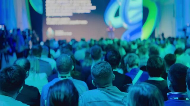 Packed conference featuring speakers on stage presenting to an engaged audience under vibrant lighting