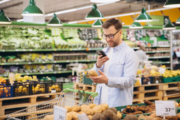 Man using smartphone and choosing potatoes in supermarket