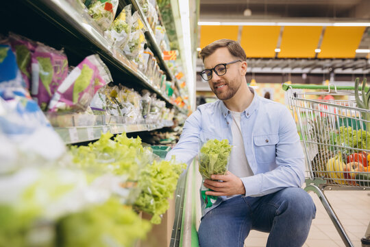 Smiling man choosing fresh lettuce in supermarket produce section