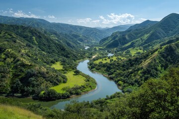Fototapeta premium Serene river winding through lush green valley under clear sky.