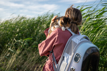 Frightened shut eyed cat hiding on woman shoulder, hugs protects pet. Owner with backpack carrier...