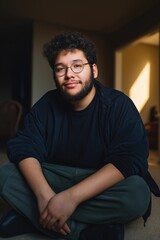 Obraz premium Young hispanic male sitting indoors with casual attire and glasses