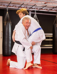 Determined black-belt older aikido practitioner in white gi honing fighting techniques during...