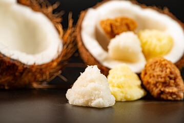 Open coconut and coconut sweets (cocadas) placed on a dark surface, black background, selective focus.