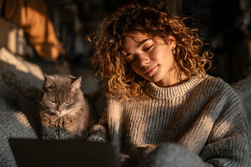 Young hispanic latin ethnic teen girl relaxing sit on comfortable sofa with cute pet cat watching remote education webinar class, movie series on laptop drinking warm tea in cozy sunny living room.