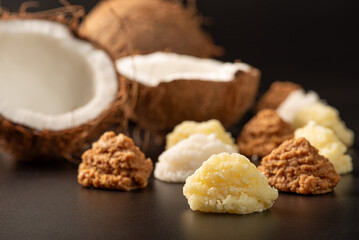 Open coconut and coconut sweets (cocadas) placed on a dark surface, black background, selective focus.