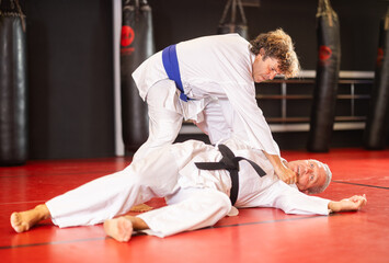 Concentrated blue-belt middle-aged aikido fighter in white gi honing fighting techniques during...