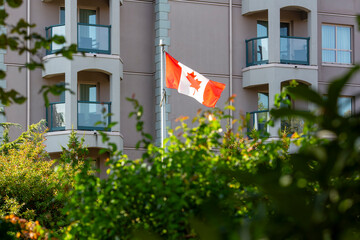 Canadian flag waving with residential building and greenery in the background.