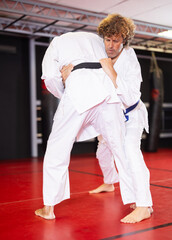 Determined motivated middle-aged man working on martial arts skills in training fight on red tatami...