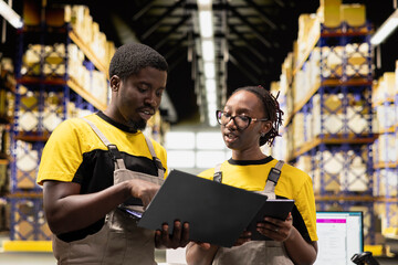 Black colleagues preparing orders in boxes for shipment in large warehouse, checking inventory on...