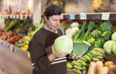 Portrait of positive satisfied man buying fresh cabbage in grocery shop