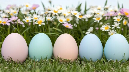 Fototapeta premium Colorful decorative eggs arranged in a row on vibrant green grass, surrounded by beautiful blooming flowers in springtime