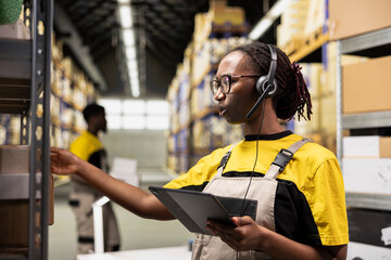 African american woman answering calls on the help line in large scale depot, handling order...