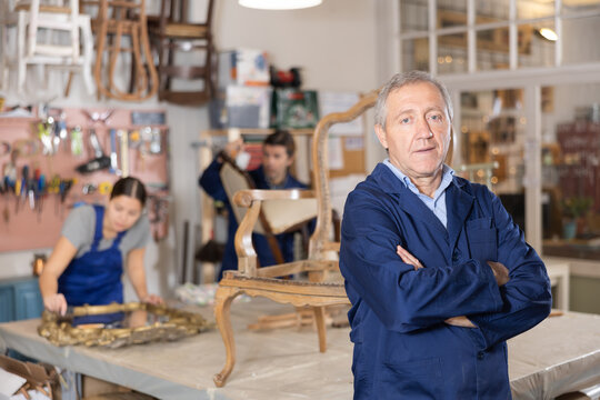 Confident mature male carpenter showing around local furniture workshop