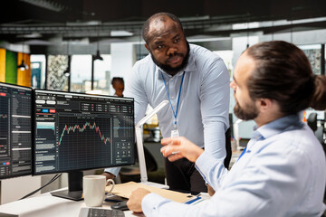 Manager supervising day trader in forex company office buying stocks to capitalize on market...