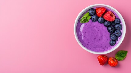 Healthy berry smoothie bowl topped with fresh strawberries, blueberries, and mint leaves against a vibrant pink background