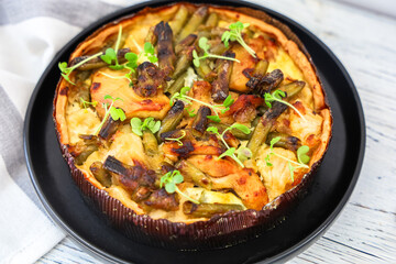 Savory vegetable tart quiche pie with fresh greens on a black plate displayed on a wooden table