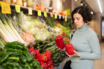 Woman carefully selects red bell peppers in a grocery supermarket