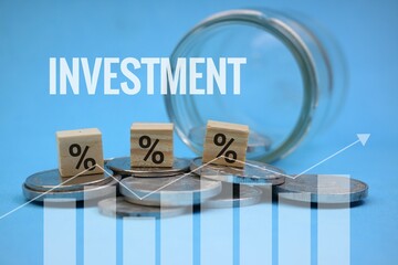 A pile of coins spilling out of a glass jar with a percentage symbol on a wooden block and a graph....
