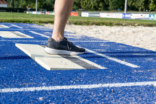 Athlete prepares for long jump on blue track surface, showcasing athletic footwear and starting board, emphasizing focus and determination