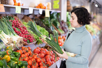 Adult woman buyer choosing fresh green onions in vegetable shop