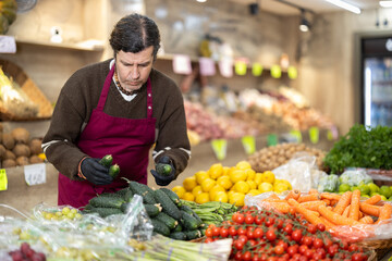 Adult man seller in apron conducting inventory with checklist in vegetable shop