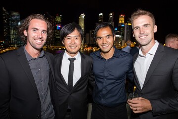 Four men pose smiling at a social event with a stunning city skyline backdrop.
