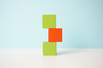 Green and orange stacked wooden blocks forming a unique arrangement on a pastel blue background,...