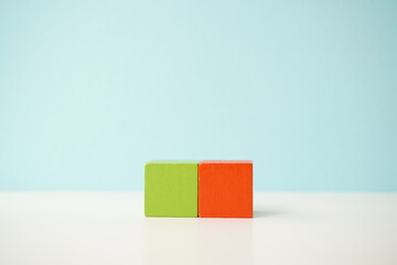 Two solid wooden blocks in contrasting green and orange colors on a light backdrop, versatile wooden cubes on clean background for business, health and education concepts.