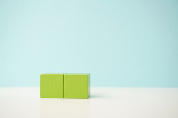 Two green wooden blocks placed together on a light blue background, versatile wooden cubes on clean background for business, health and education concepts.