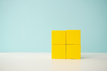 Four yellow wooden blocks arranged in a square, isolated against a soft blue backdrop, showcasing versatile wooden cubes on clean background for business, health and education concepts.