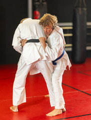 Determined motivated middle-aged man working on martial arts skills in training fight on red tatami...
