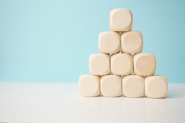 Pyramid arrangement of smooth, natural wooden cubes against a soft blue background, versatile wooden cubes on clean background for business, health and education concepts.