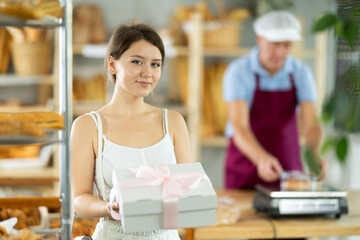 Portrait of young girl buyer with gift box of fresh baked goods in interior of a bakery