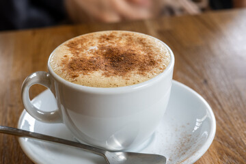 Cappuccino with Cinnamon Powder in White Cup on Wooden Table