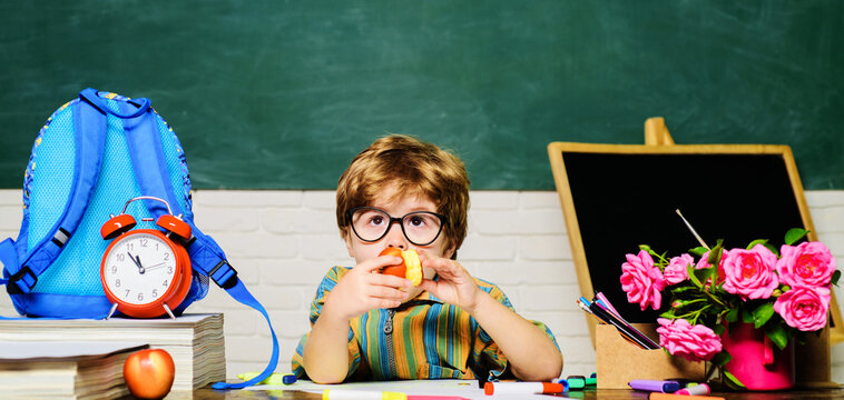 School lunch. Cute schoolboy in glasses sitting at desk and eating apple. Delicious food for kids health. Boy eats apple during lunch break. Little schoolboy eating apple in classroom. Back to school.