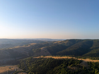 Aerial drone view of a vast landscape in Turkey featuring rolling hills covered with dense forests and open fields under a clear blue sky, highlighting the beauty of rural nature.