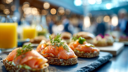 Smoked salmon on toast with dill, arranged on a platter. Orange juice glasses and other foods are in the blurred background.