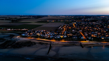 Coastal evening aerial view of illuminated village by sea.